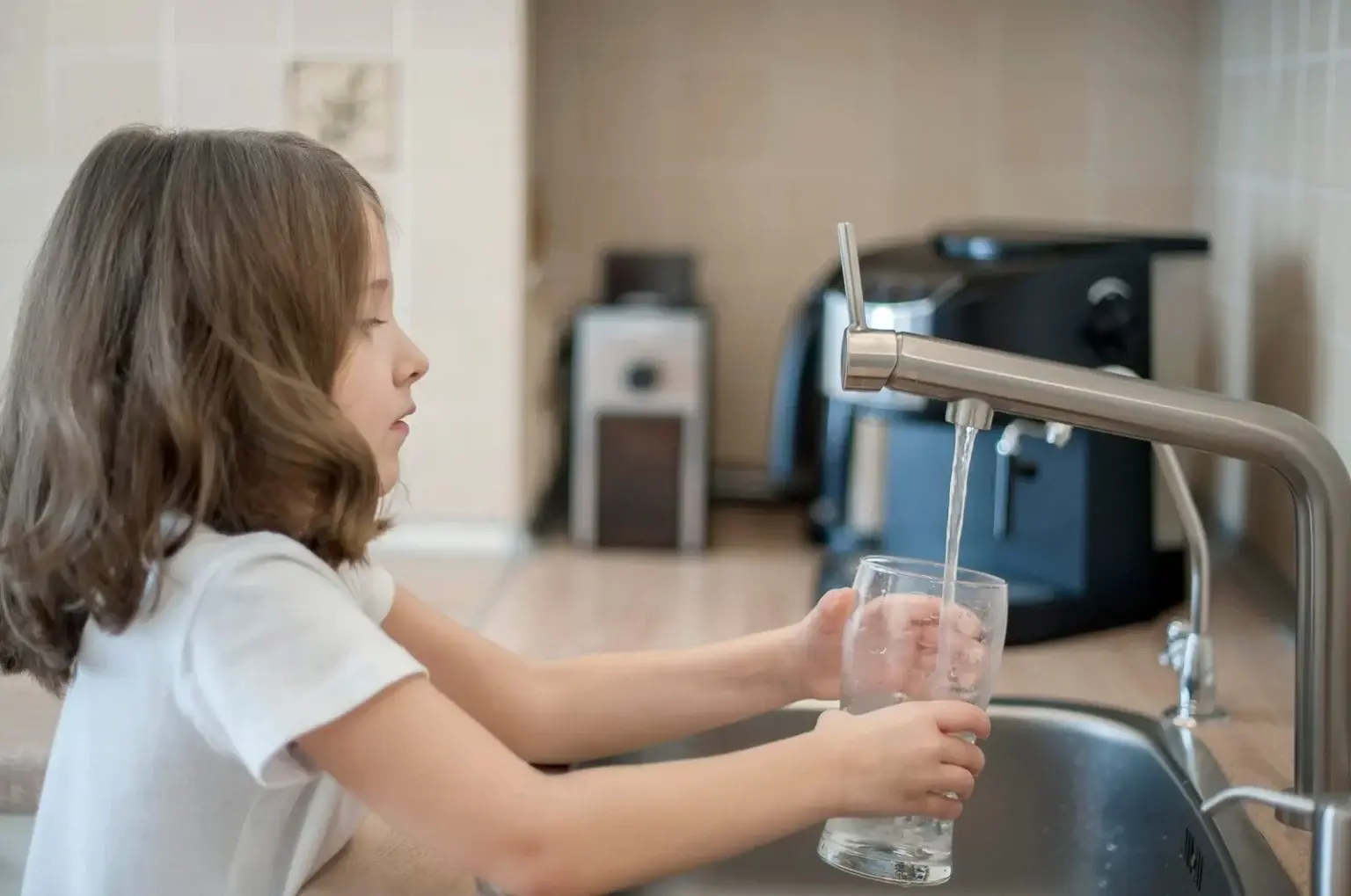 Girl filling glass with water from tap.